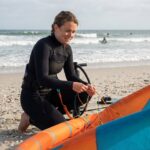 Jeune femme en wetsuit ajustant son cerf-volant de kitesurf sur la plage