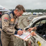 Pilote et copilote de rallye consultant le calendrier des manches 2026 mis à jour dans le paddock du service park