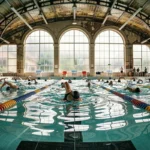 Piscine intérieure municipale parisienne avec nageurs de club s'entraînant dans les couloirs lors d'une séance matinale à la piscine Butte aux Cailles